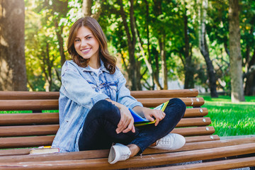 Obraz premium Young girl student sits on a bench in the park and holds books, notebooks. Girl teaches lessons in the park.