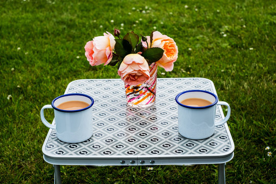 Two enamel mugs of tea and flower vase placed on picnic table