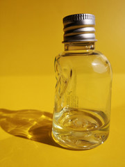 Slightly crumpled plastic bottle or jar with transparent liquid. Abstract close-up photo of deformed or distorted packaging design on dark yellow or golden color background with space for text. 