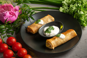 pancakes with cream and sour cream decorated with greens and tomatoes in a black plate