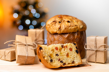 Delicious Panettone slice with candied fruits with blinking blurred christmas lights. Dry fruits. Gifts scattered on the table.