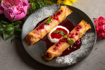 pancakes stuffed with cottage cheese with sour cream and lingonberry sauce in a black plate
