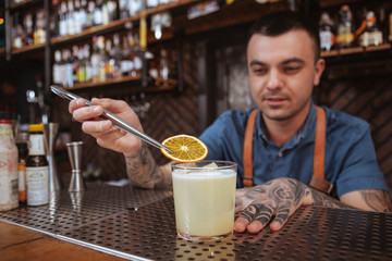 Professional bartender garnishing cocktail with a slice of orange