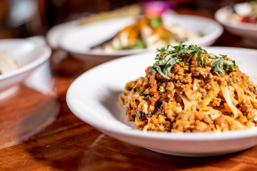 Bolognese handmade spaghetti topped with fresh basil in a white bowl on wood table
