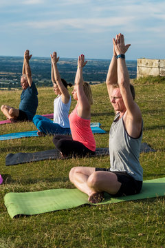 Group of women and men taking part in yoga class on hillside