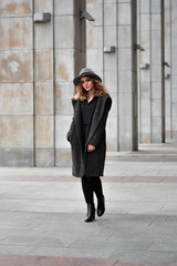 Fototapeta na wymiar Portrait of beautiful woman with blond hair wearing hat and gray coat. Outdoor full length photo in city