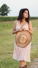 Woman walking through a field in cowgirl boots with cow girl hat and pink dress on