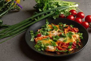 fried eggs with tomatoes and herbs in a black plate
