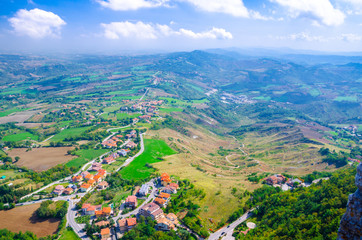 Aerial top panoramic view of landscape with valley, green hills, fields and villages of Republic San Marino suburban district with blue sky white clouds background. View from San Marino fortress