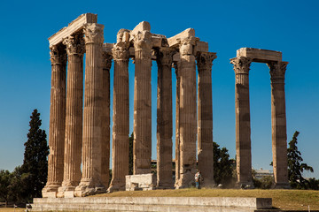 Man using a scythe to cut the grass at the ruins of the Temple of Olympian Zeus in Athens