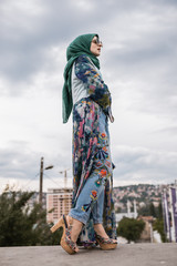 Outdoor romantic portrait of young European Muslim woman with hijab have fun and posing for camera. Image of pretty model wearing maxi dress, green scarf, sunglasses and heels.Fashion editoral concept