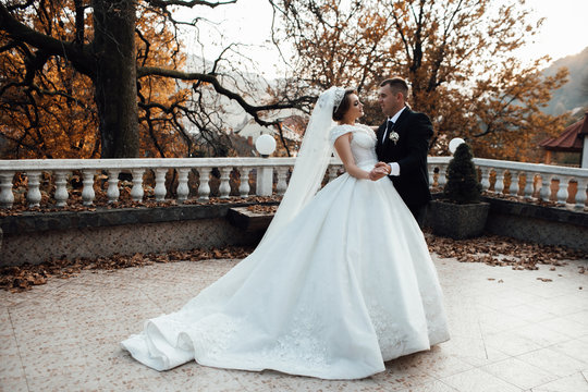 Couple ready to give a kiss, smiling at each other in the sunset. Wedding couple in autumn. Pretty bride and stylish groom. Photo of a young couple posing in wedding suite and dress with a plume