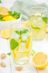  Homemade lemonade with lemon slices, mint and brown sugar in a glass with ice on a white wooden background.