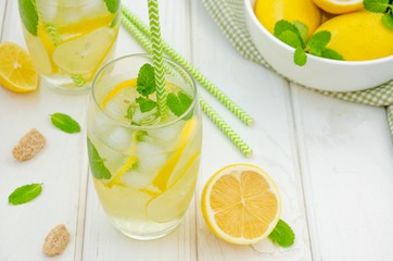  Homemade lemonade with lemon slices, mint and brown sugar in a glass with ice on a white wooden background.