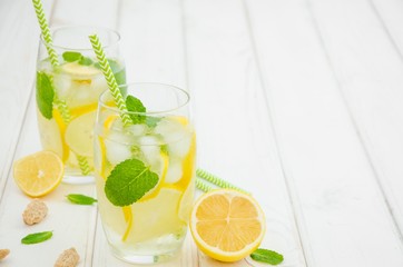 Homemade lemonade with lemon slices, mint and brown sugar in a glass with ice on a white wooden background.