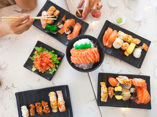 Top view of japanese traditional food A set of sushi rolls on a table in a restaurant , hand of people eating sushi rolls using bamboo sticks.