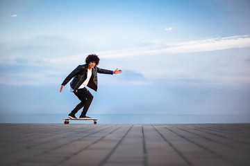 Young afro american man skateboarding in front of big blue sky