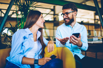 Obraz premium Male and female bloggers enjoying meeting together and communicating with followers in social networks via smartphone devices, two happy hipsters talking to each other in break of using gadgets