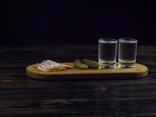 Obraz na płótnie Canvas two misted glasses with cold vodka on a wooden board with bacon and pickled cucumbers. traditional russian snack