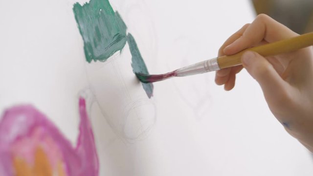 Closeup of kid's hand paints a picture on canvas. Children's creativity