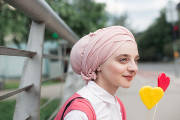 romantic portrait of young European Muslim woman with hijab have fun at beautiful sunny day. Image of pretty woman playing with two heart shaped lollipops. She is happy and relaxed.