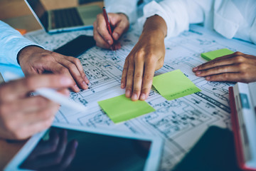Cropped image of female hand putting stick with notes on blueprint during collaboration with male...