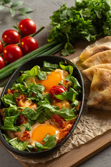 fried eggs with tomatoes and herbs in an oval black dish