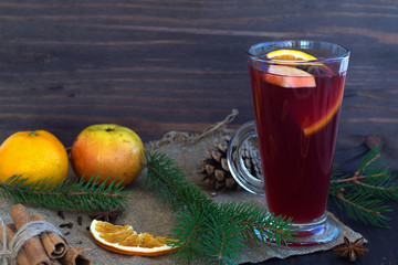 glass of mulled wine with slices of orange, apple and spices, cinnamon and anise star on a wooden...