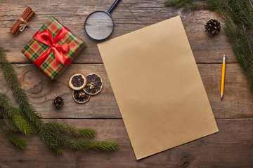 A wish list. Old paper sheet with pencil at grunge wooden background with copy space. Christmas tree, gift, cones, dried citrus fruits, magnifying glass, cinnamon