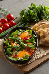 fried eggs with tomatoes and herbs in an oval black dish
