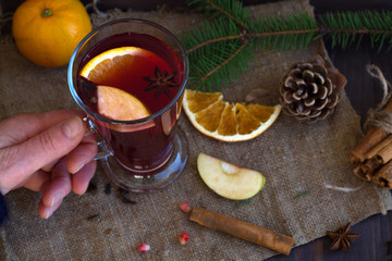 woman's hand holding a hot mulled wine with slices of orange, apple and spices, cinnamon and anise...