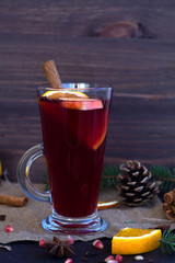 hot mulled wine with slices of orange, apple and spices, cinnamon and anise star on a dark wooden table with winter decorations. hot drinks of winter and autumn. vertical