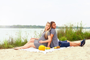 Pregnant girl and guy on a picnic by the river