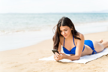 Fototapeta na wymiar Young Female Using Mobile Phone On Sea Shore