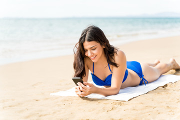 Fototapeta na wymiar Happy Female In Bikini Using Phone At Beach