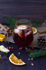 Winter and autumn hot drinks. Glass of red hot mulled wine in the centre with apple and spices with sticks cinnamon on a wooden table with slices of orange. vertical. 