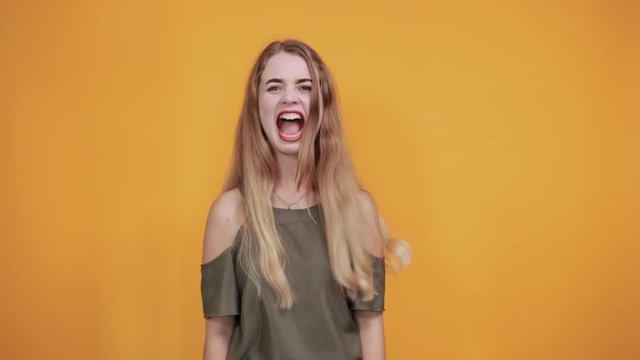 Crazy young woman in shirt smiling, growling like animal, making cat claws gesture isolated on orange background in studio. People sincere emotions, lifestyle concept.