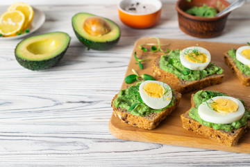 Healthy toasts with whole grain bread, avocado and boiled egg on wooden board.