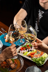 People clink glasses with white wine above a table full of meals in a restaurant