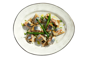 Appetizing herring in slices with green onions on a plate. Top view. Isolated over white background.