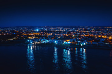Fototapeta na wymiar Aerial panoramic view of Paphos, Cyprus seaside from above at night from drone. Beautiful evening mediterranean seascape with illuminated buildings and reflections of lights in sea water.
