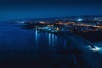 Fototapeta na wymiar Aerial panoramic view of Paphos, Cyprus seaside from above at night from drone. Beautiful evening mediterranean seascape with illuminated buildings and reflections of lights in sea water.