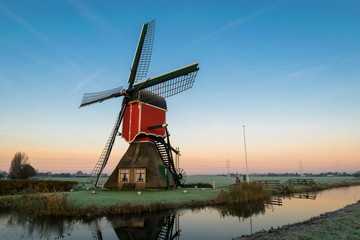 Naklejka premium Stunning landscape image of a traditional dutch windmill at sunrise on a cold morning in autumn