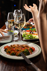 People having dinner in a restaurant with white wine and grilled chicken with vegetables on foreground