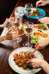 People having dinner in a restaurant with white wine and grilled chicken with vegetables on foreground
