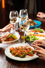 People having dinner in a restaurant with white wine and grilled chicken with vegetables on foreground