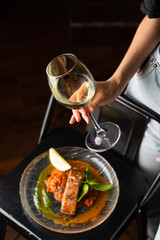 Woman is standing at the table with marinated chum salmon on it,  holding a glass of white wine and fork