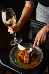 Woman is standing at the table with marinated chum salmon on it,  holding a glass of white wine and fork