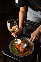 Woman is standing at the table with marinated chum salmon on it,  holding a glass of white wine and fork
