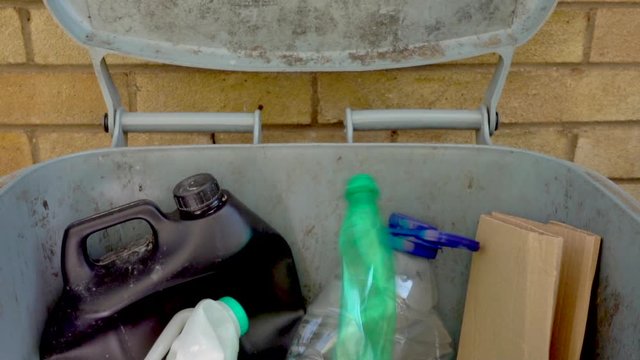 Close shot of various household waste items dropping into a recycling / recyclable bin.